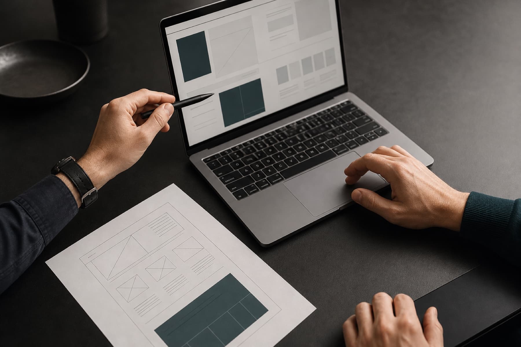 Two professionals collaborating over a laptop and a precise website wireframe